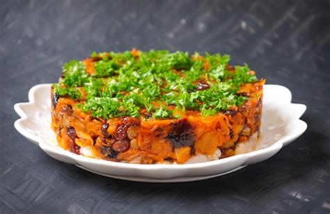 šviežiai paruošta silkė su džiovintais vaisiais ir daržovėmis, patiekta lėkštėje su garnyru